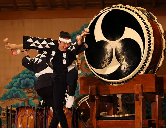 a man plays a taiko drum with a smile