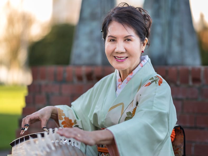 Masumi Timson dressed in a light green kimono posed with her koto outside