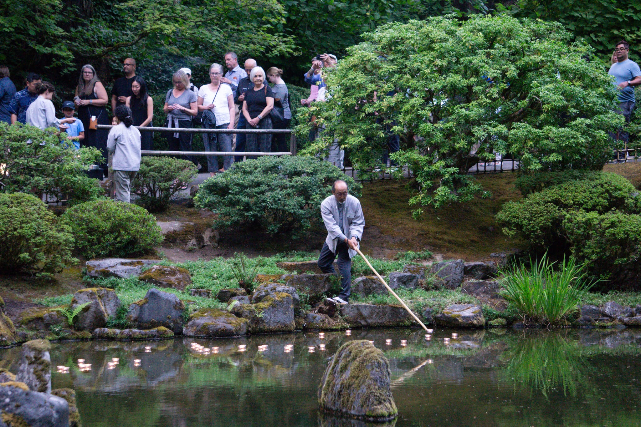 Japanese man setting candles into water with a bamboo stick for obon festival
