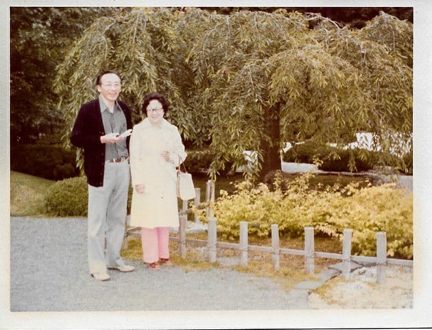 A husband and wife in the either 1970s or 80s standing next to a weeping cherry tree