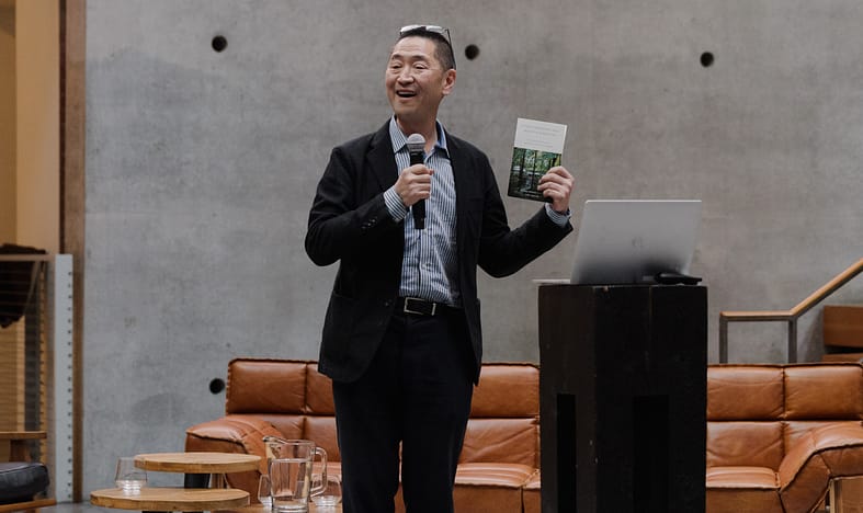 Ken Tadashi Oshima standing and talking into a microphone.