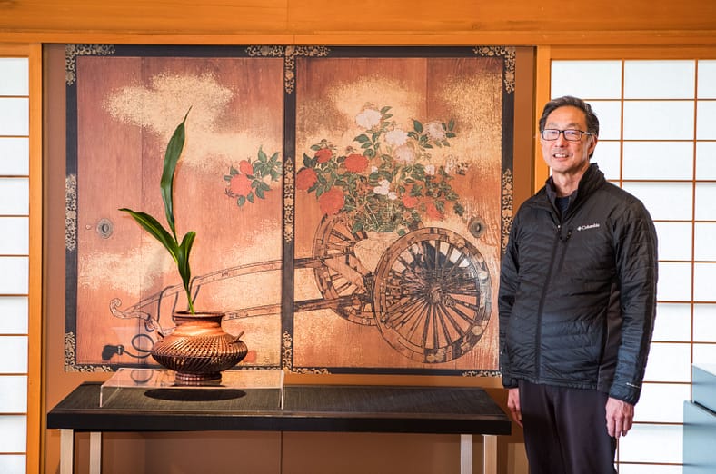 a man smiling next to a display of ikebana