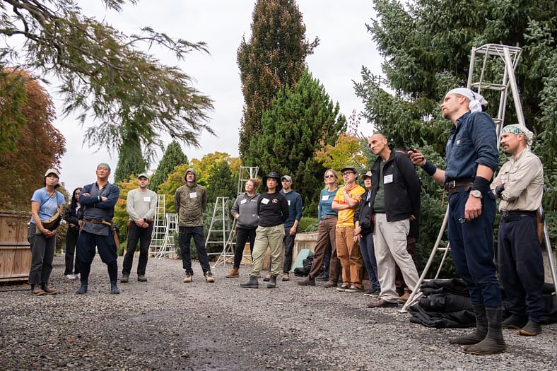 a group of people looking at a gardener pointing at a tree