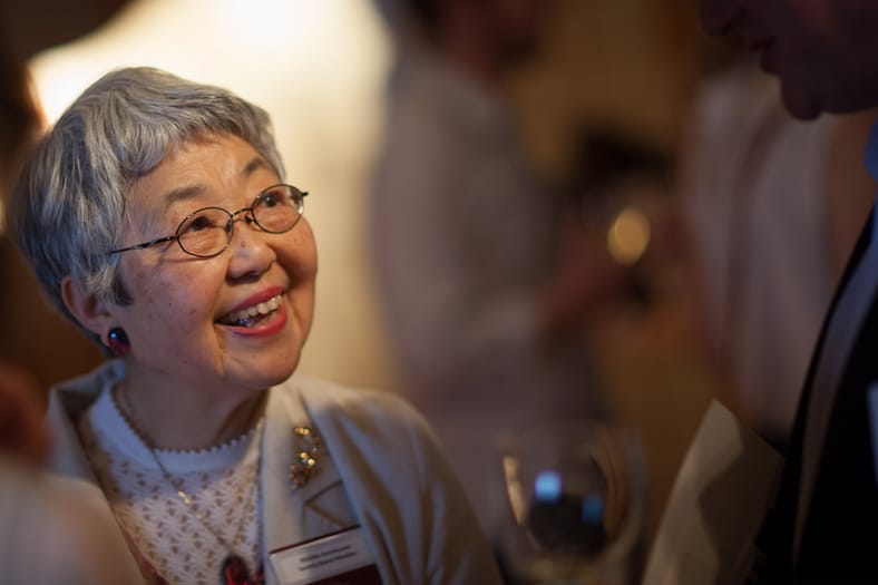 a woman with short gray hair and glasses smiles looking to someone off camera