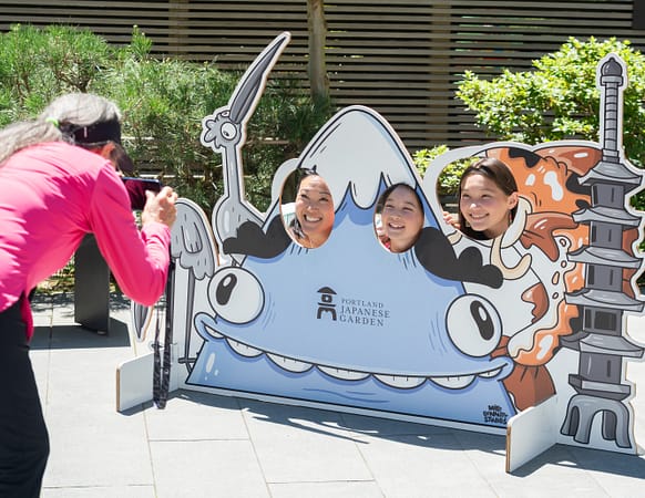 a family sticks their faces in through holes in a large photo standee featuring a cartoon Mt. Hood