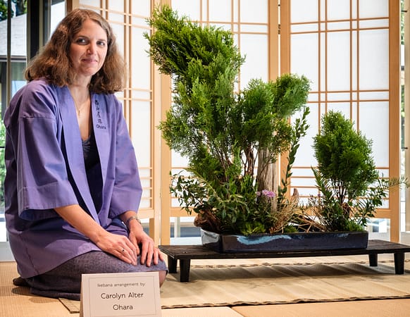 A woman sits next to ikebana.