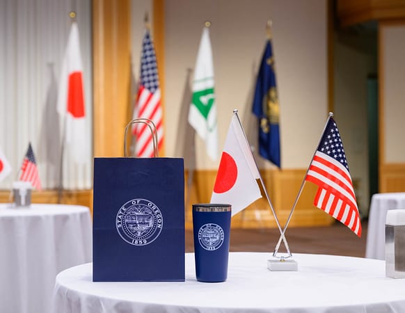a table with a bag that has the Oregon state logo on it and two flags, one American and one Japanese