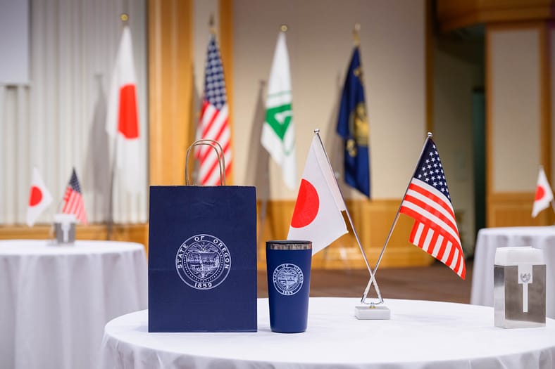a table with a bag that has the Oregon state logo on it and two flags, one American and one Japanese