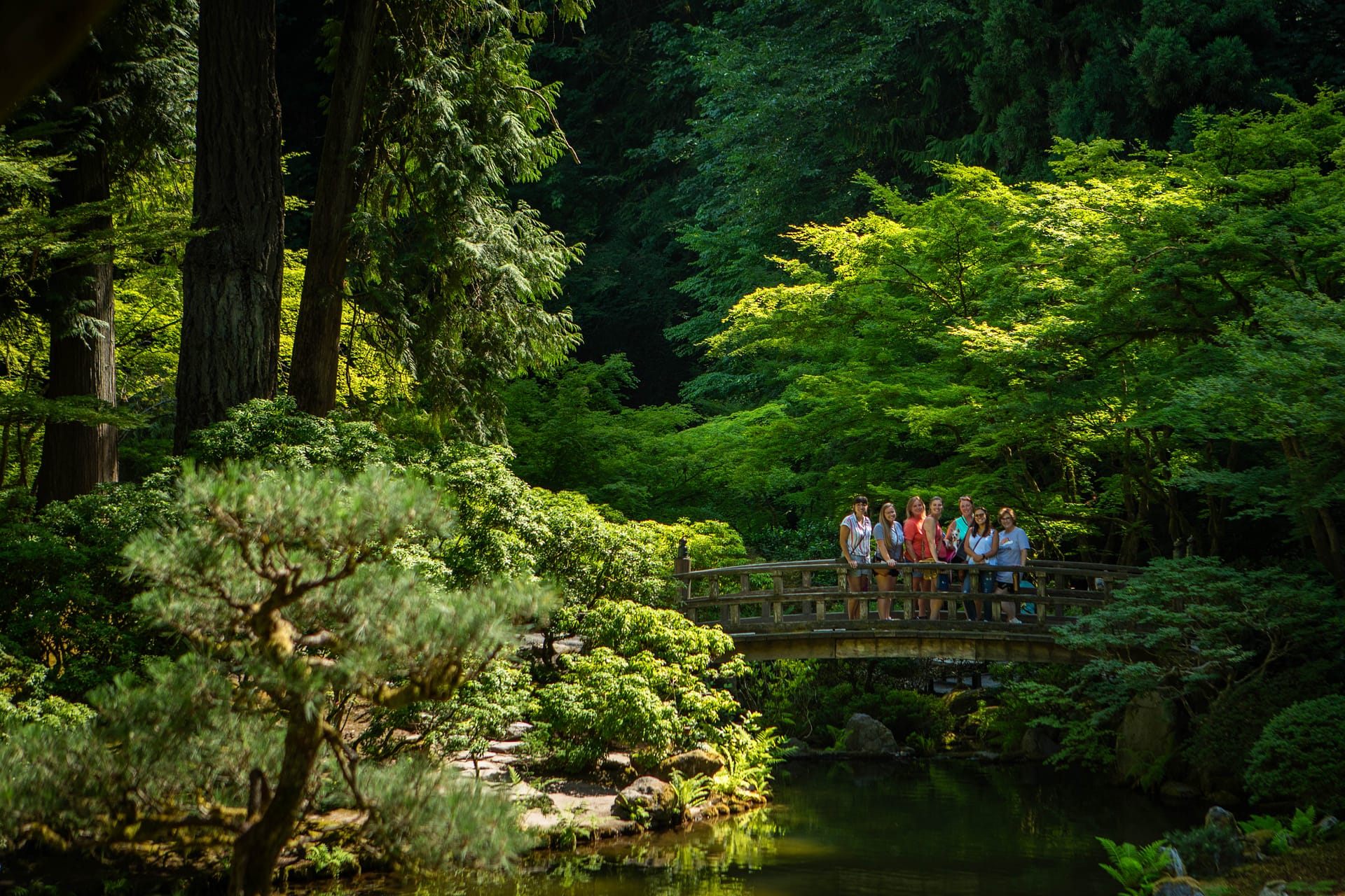 A fair away shot of people smiling and standing on a wooden bridge.
