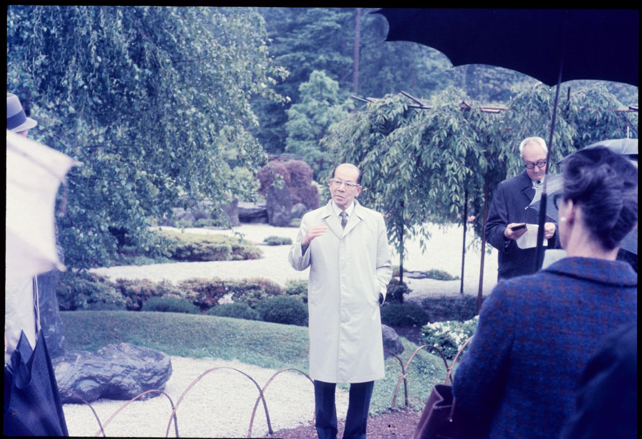 A man in a rain coat speaks to a crowd.