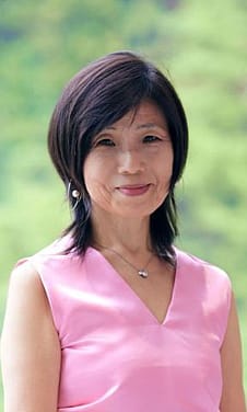 Portrait of Yuko Hasegawa in front of green out of focus foliage wearing a pink shirt