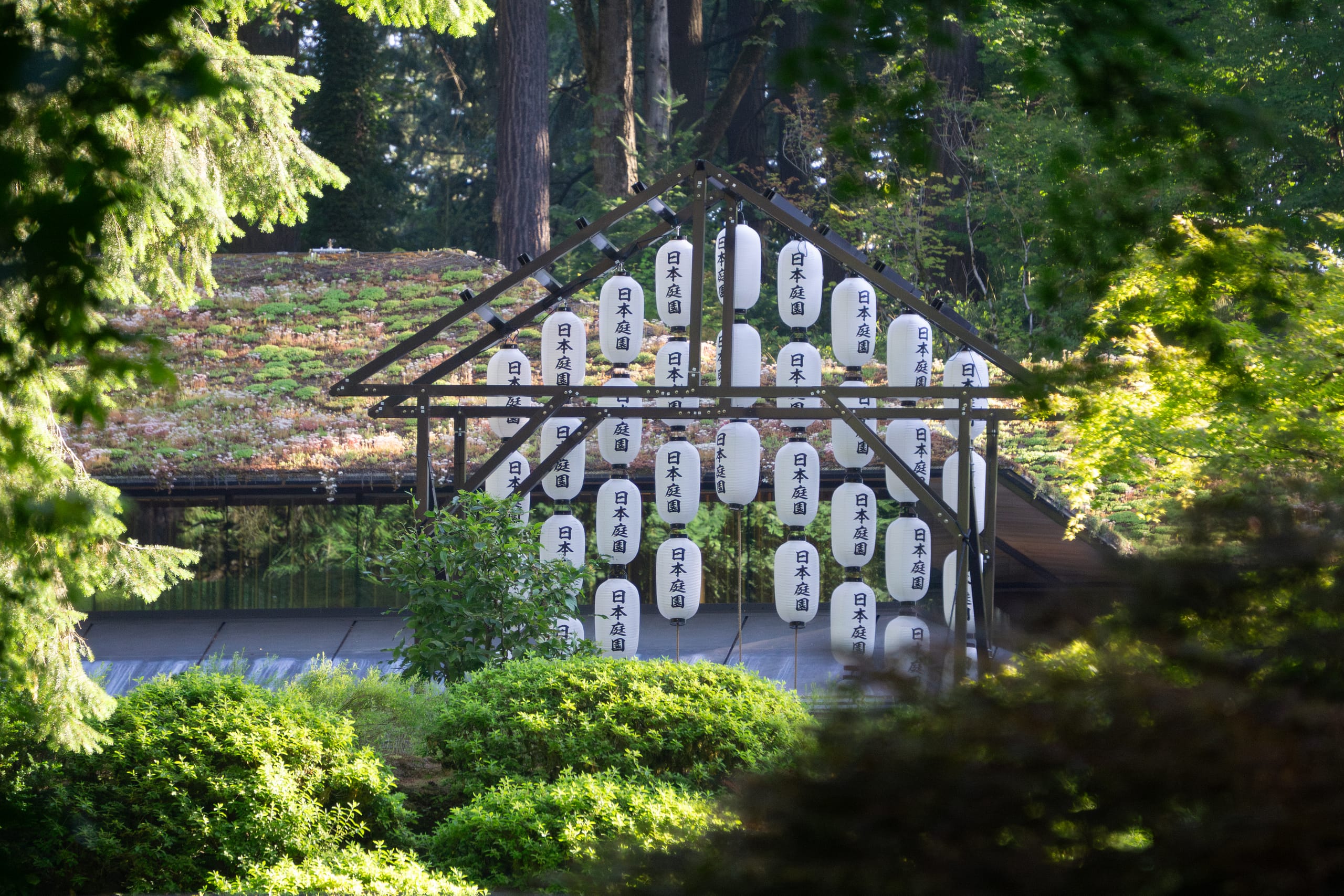 white lanterns that read "nihon teien" in Japanese hang from a metal structure in the shape of a house
