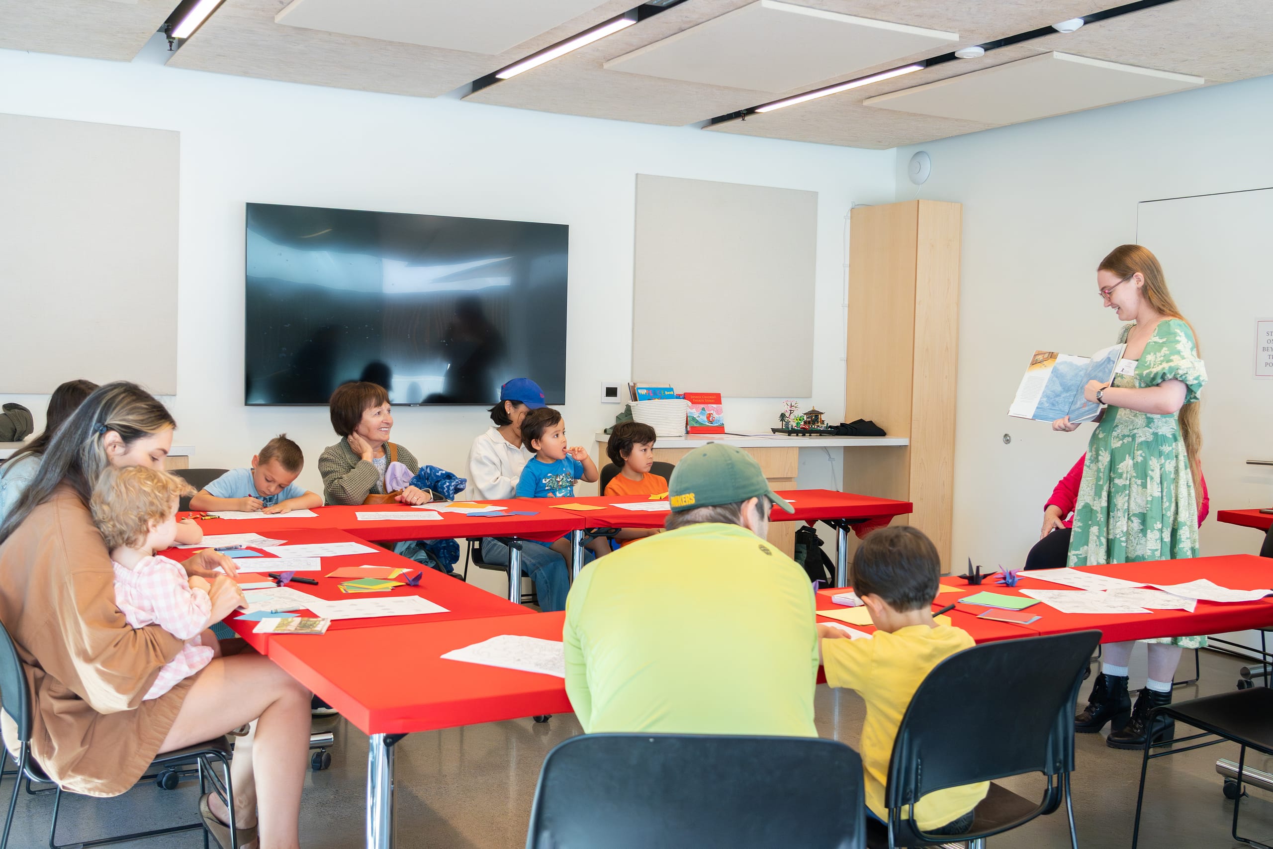 A young girl reading a book to children in a classroom.