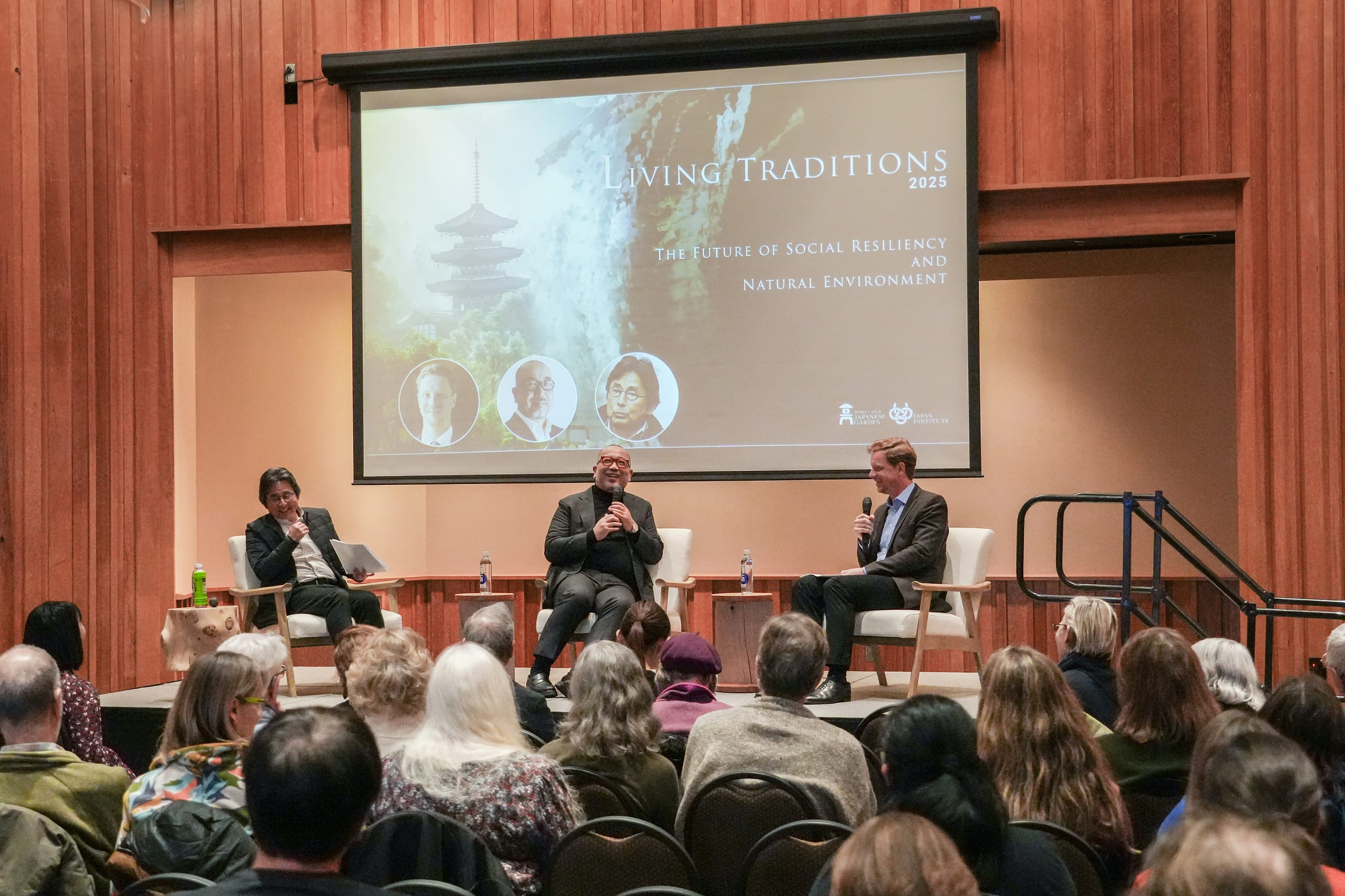 Three people sitting in chairs on stage in front of an audience.
