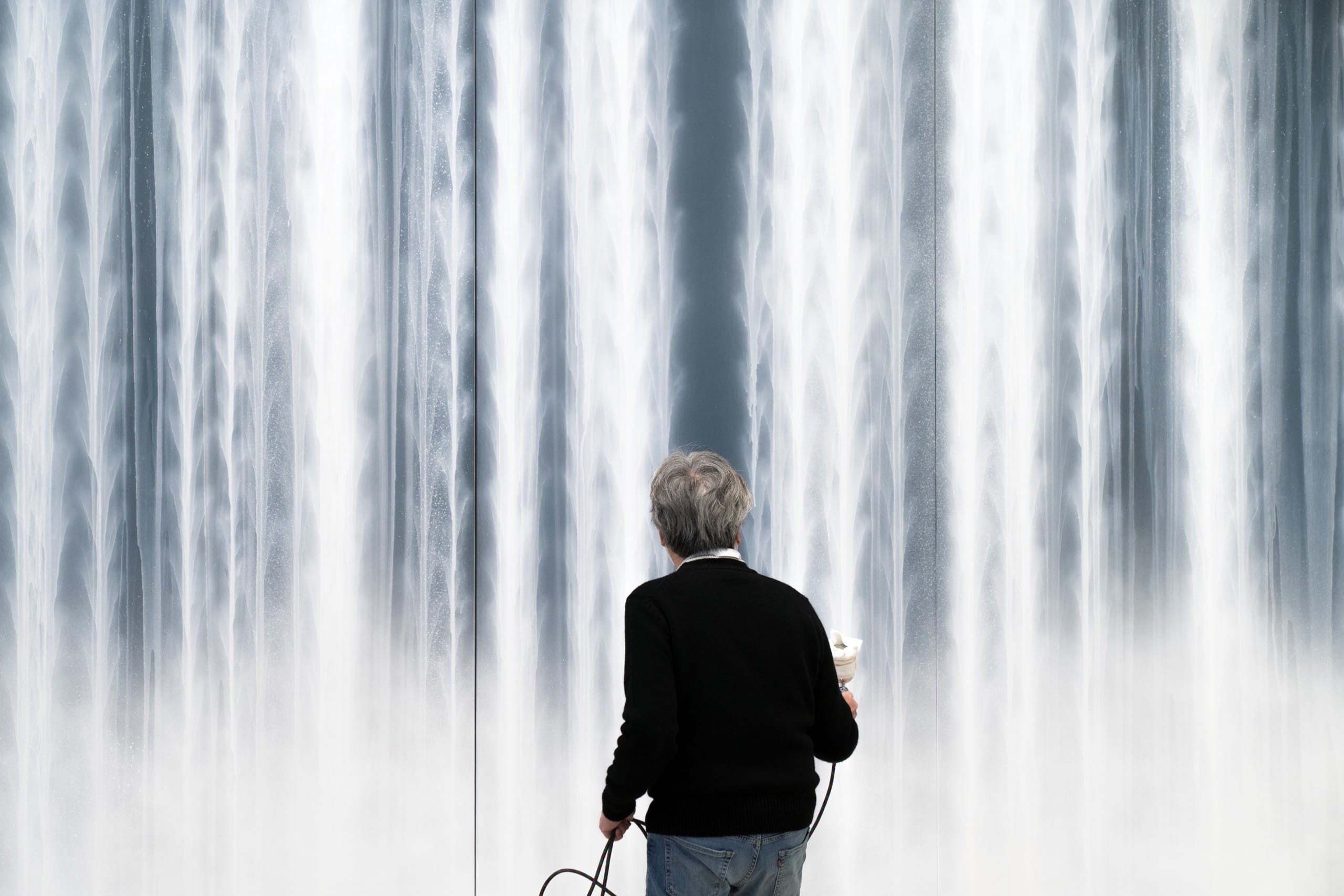 A man has his back to the camera, as he works on a large painting.