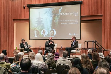 Three people sitting in chairs on stage in front of an audience.