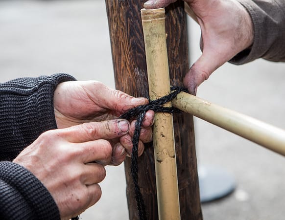 Two pairs of hands construct a bamboo fence