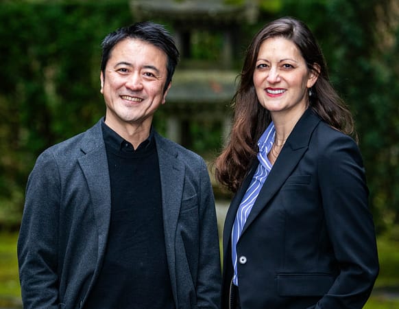 two people standing and smiling in front of a tall stone lantern