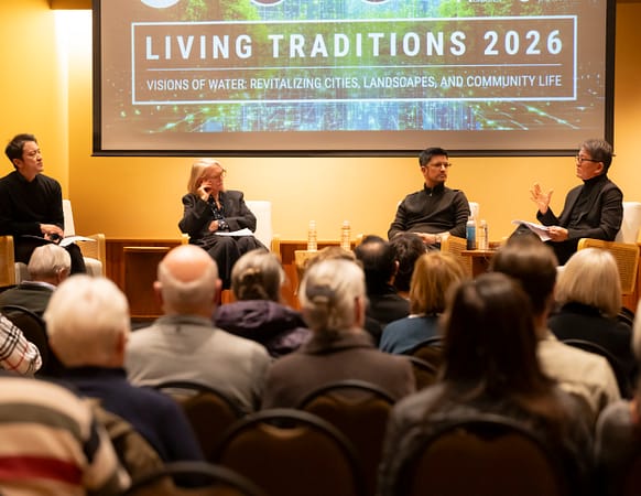 four people sitting down in chairs, chatting, in front of an audience