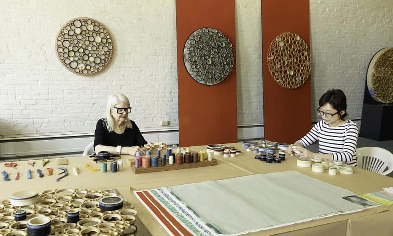 two women sitting a table with art supplies in front of them