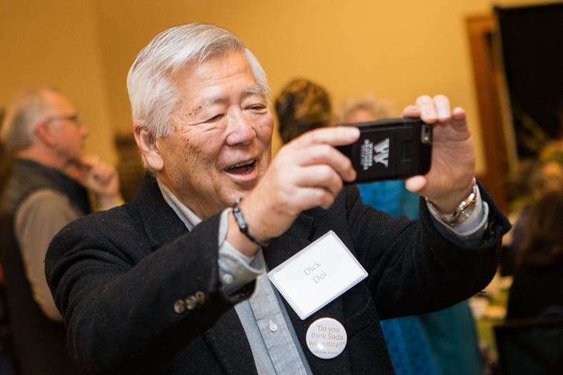 a man smiling, taking a photo with his cellphone