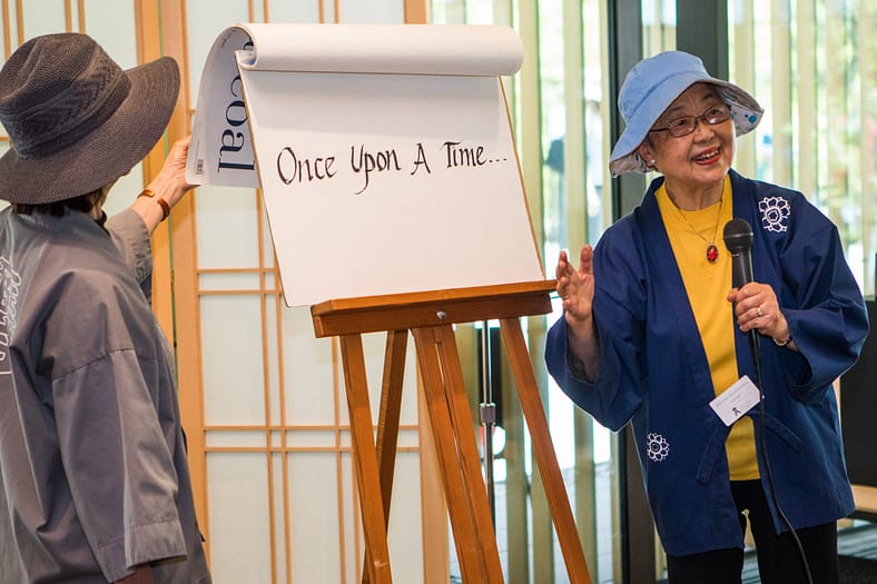 a woman with a bucket hat and hapi coat pointing to a large flipbook that says "once upon a time" on it.