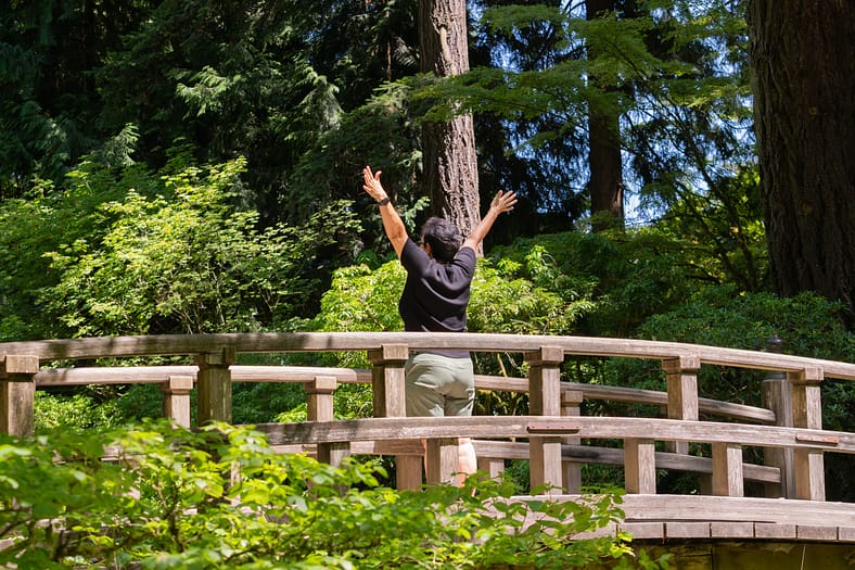 A person holds up their hands in joy while standing on a wooden bridge.