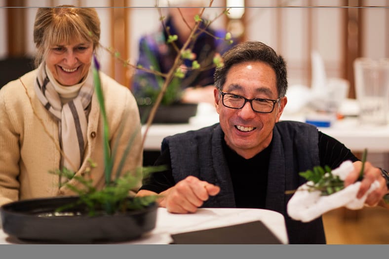 a woman smiles as a man crouches down next to her to provide instruction
