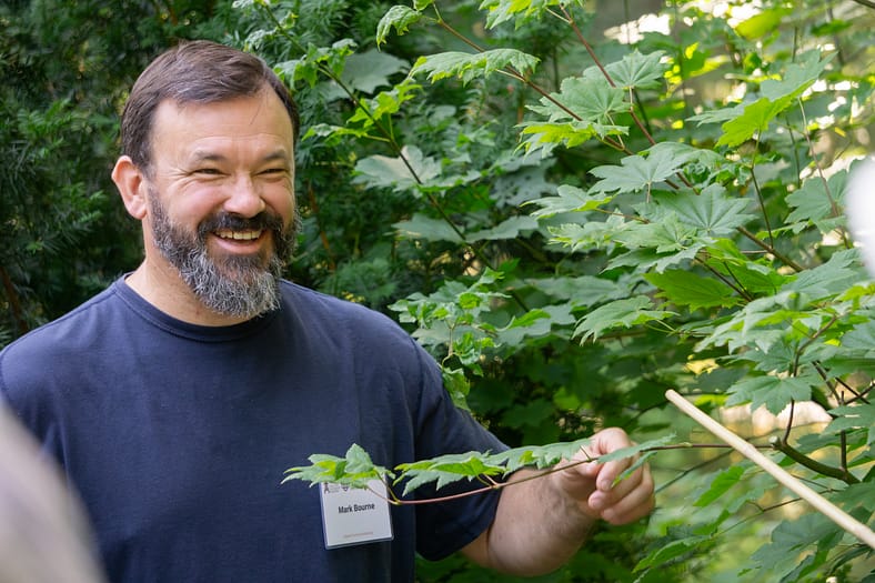 a man smiling in front of green leafs
