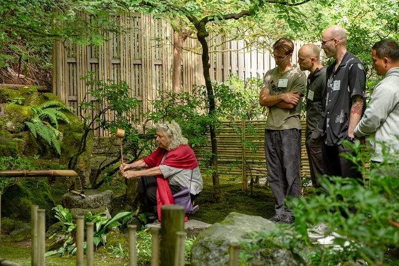 a woman crouching down at a water basin as onlookers carefully watch