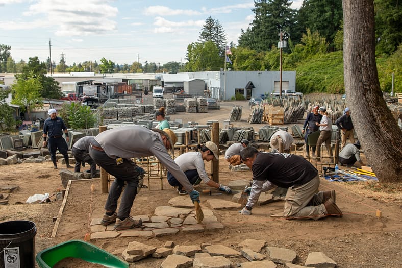 People spread out across a stone yard working on making paths