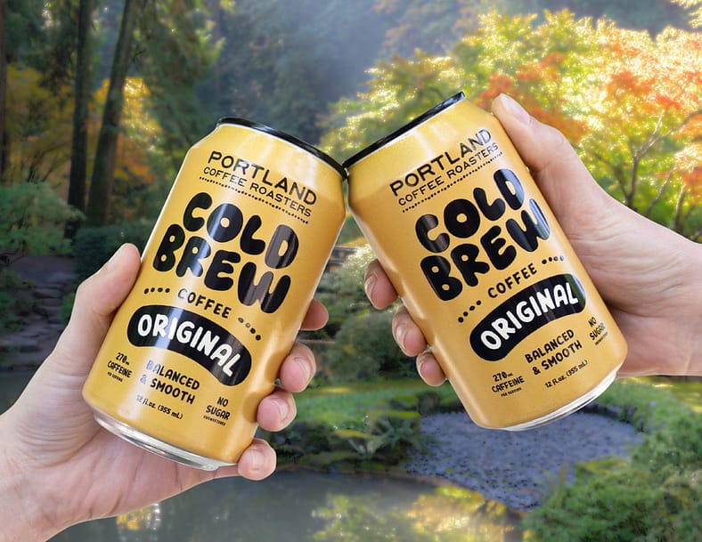 Two separate hands holding two cans of cold brew in front of the Portland Japanese Garden.