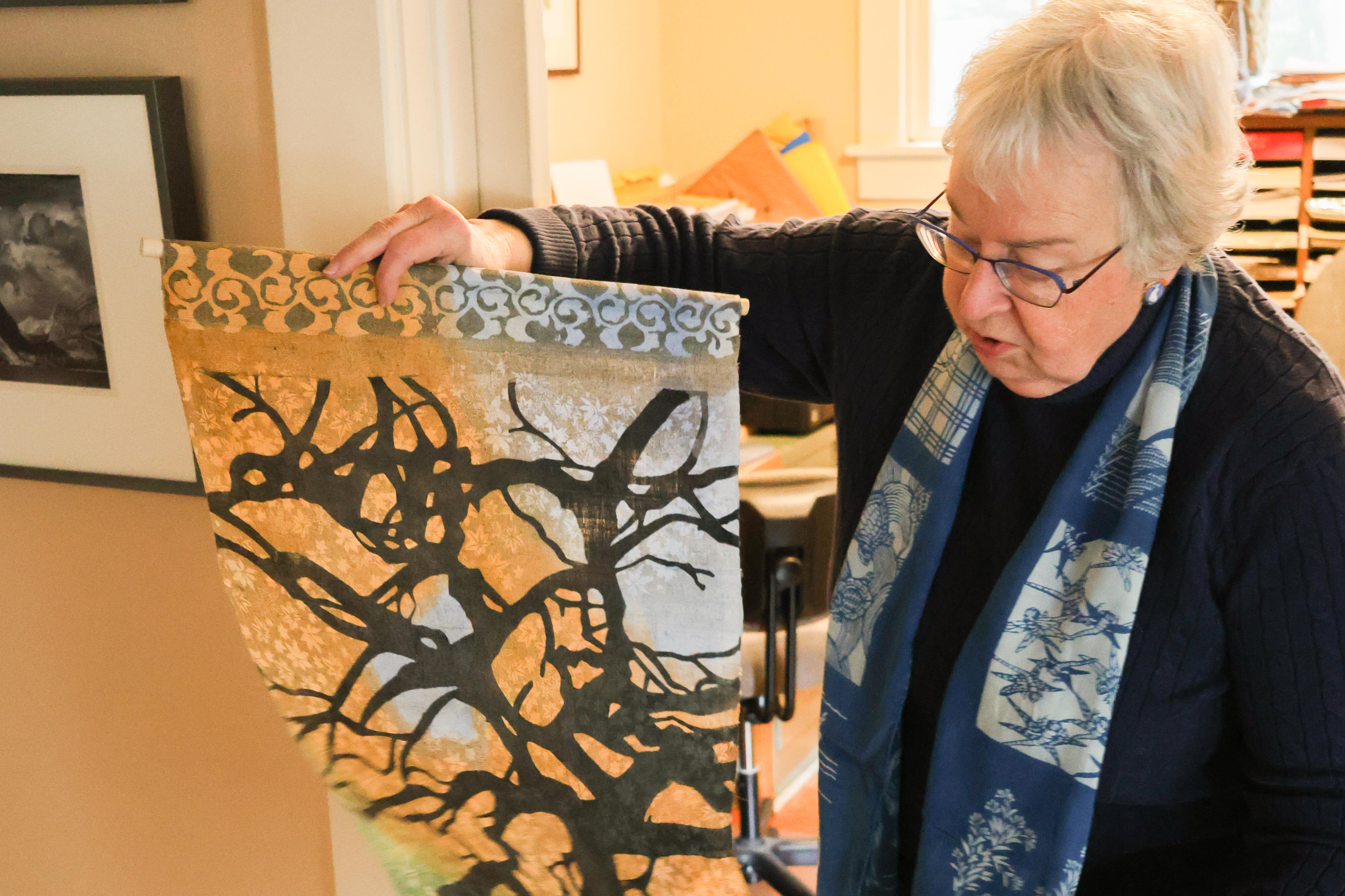 a woman holds fabric with a stencil dyed image of a tree on it