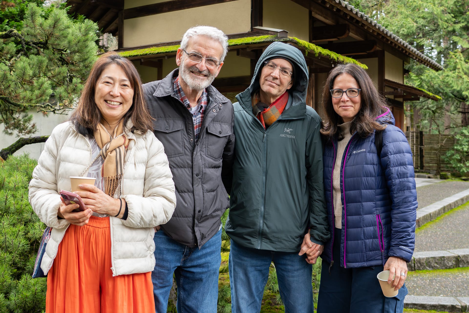 Four people smiling for a camera in front of a wooden gate house.