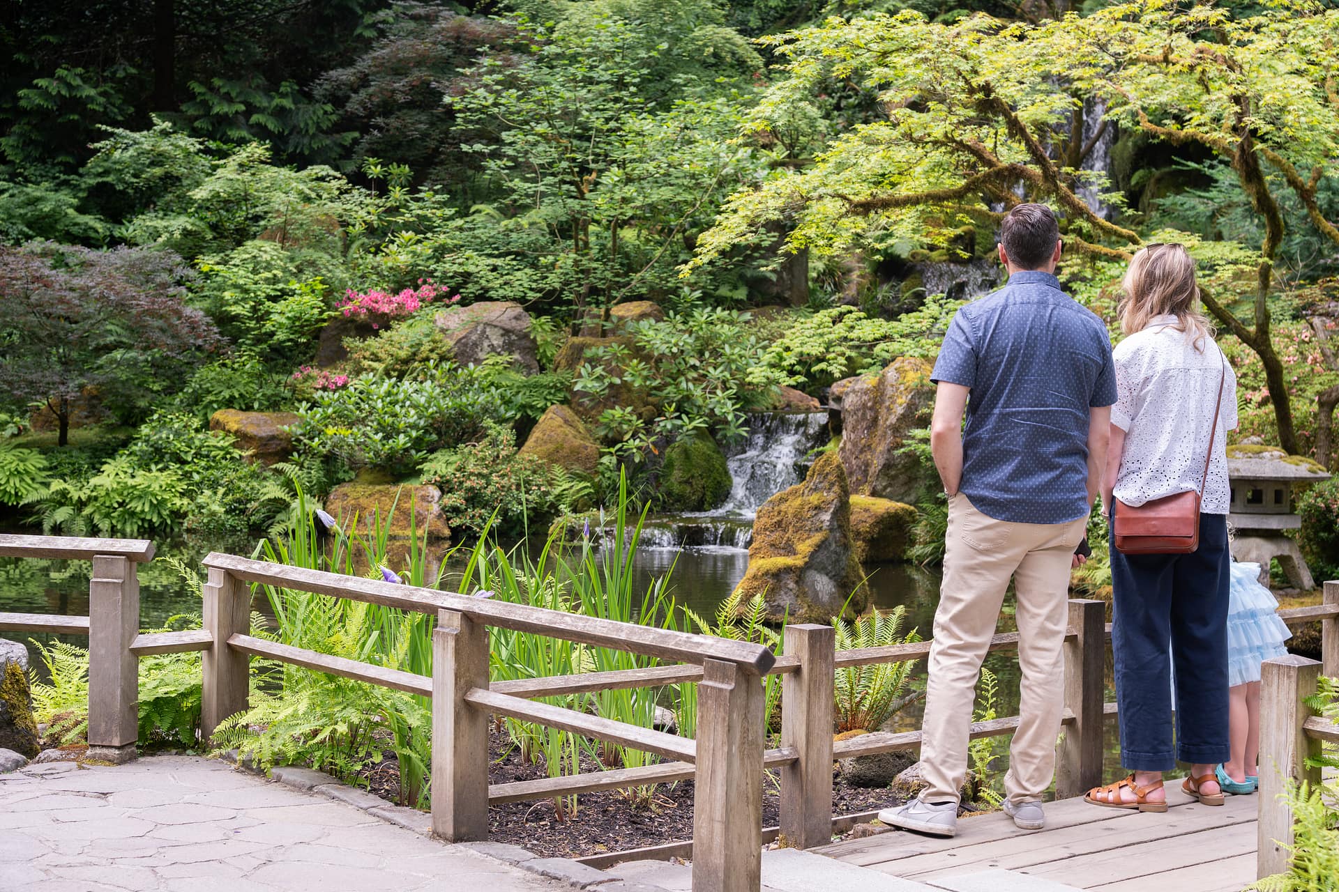 Two parents and a small child standing on a wooden bridge looking at a waterfall.