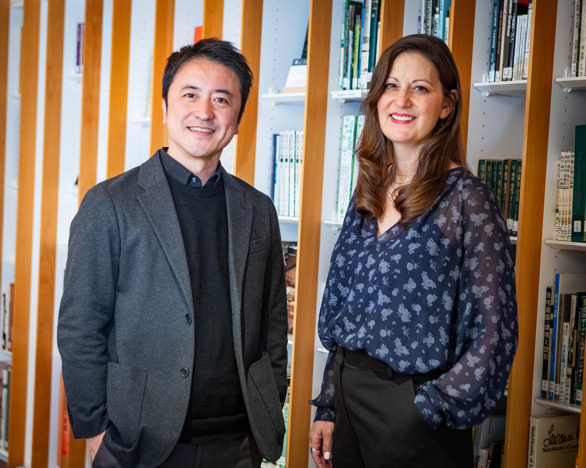 two people standing and smiling in front of a book shelf in a library
