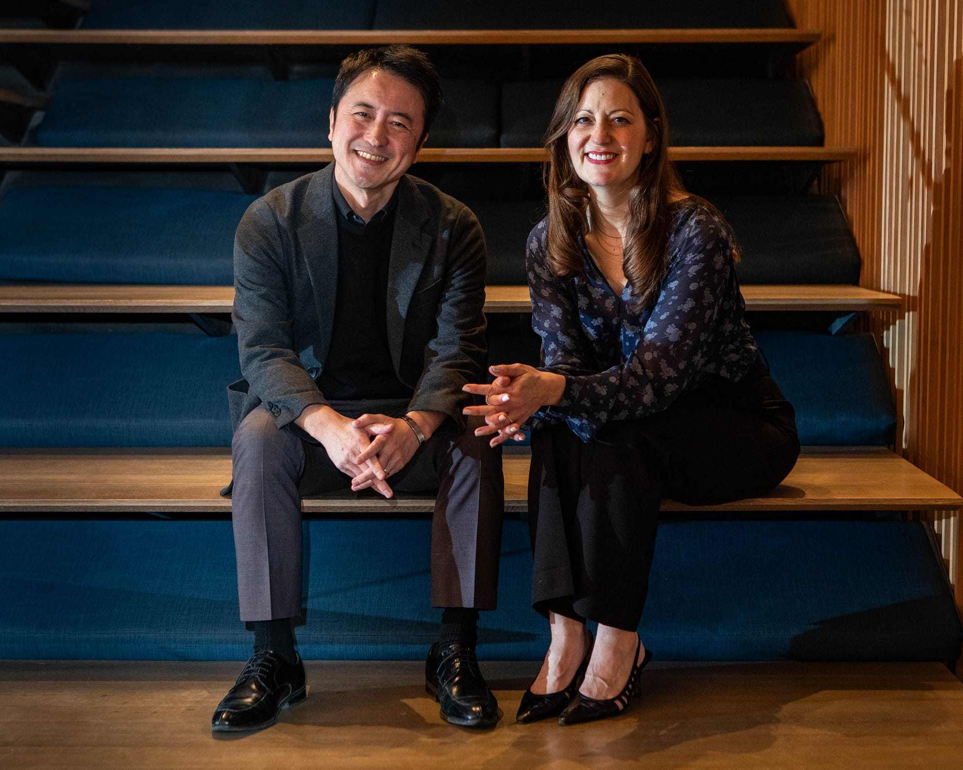 Two people sitting on wooden stairs, smiling for the camera.