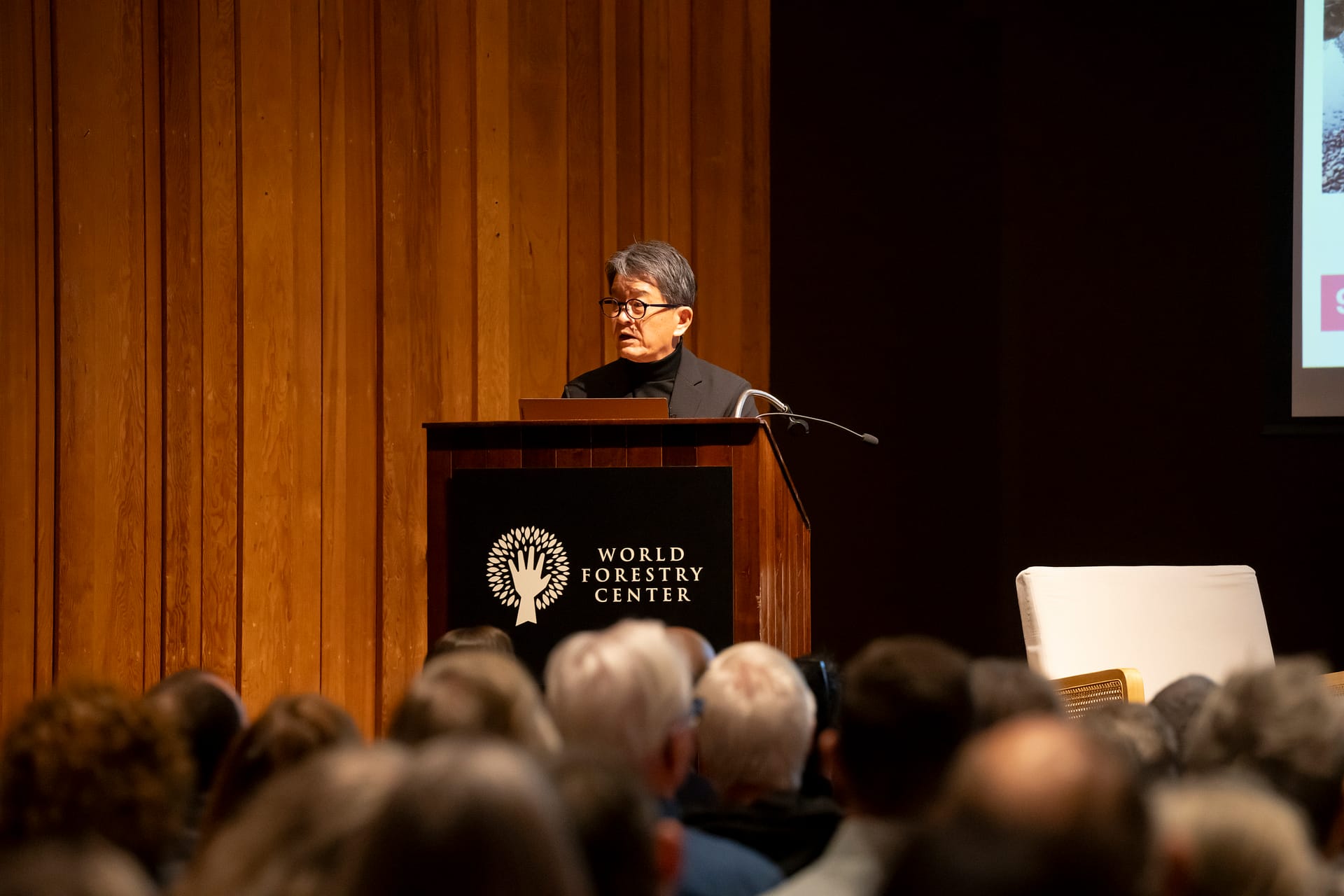 A man speaking behind a podium to a seated audience.