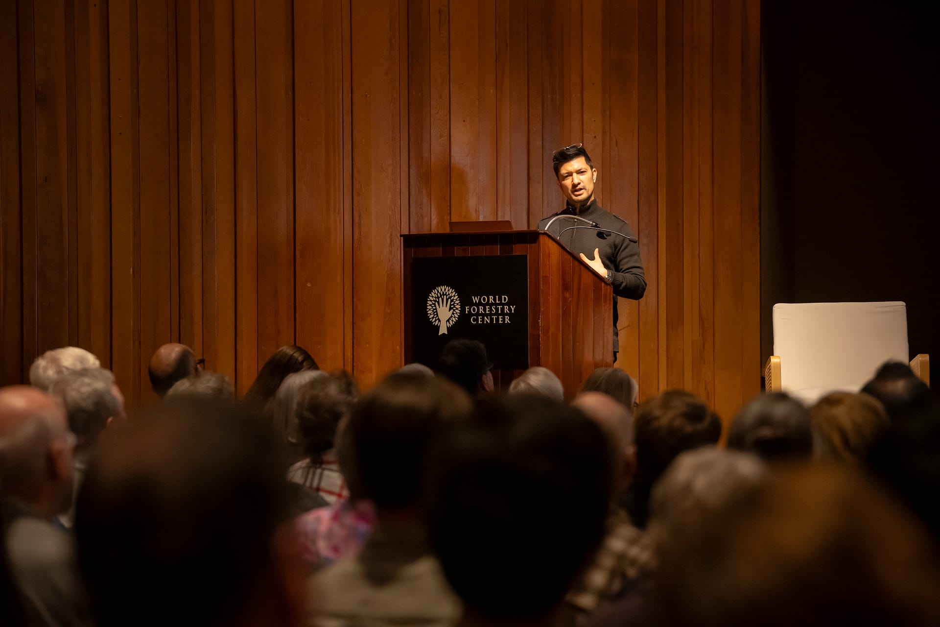 A man speaking behind a podium to a seated audience.