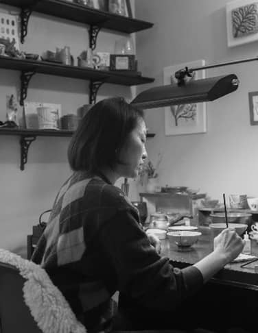 a woman sits at a desk with a paintbrush