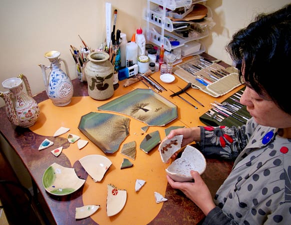 a woman piecing together broken pottery in her home studio