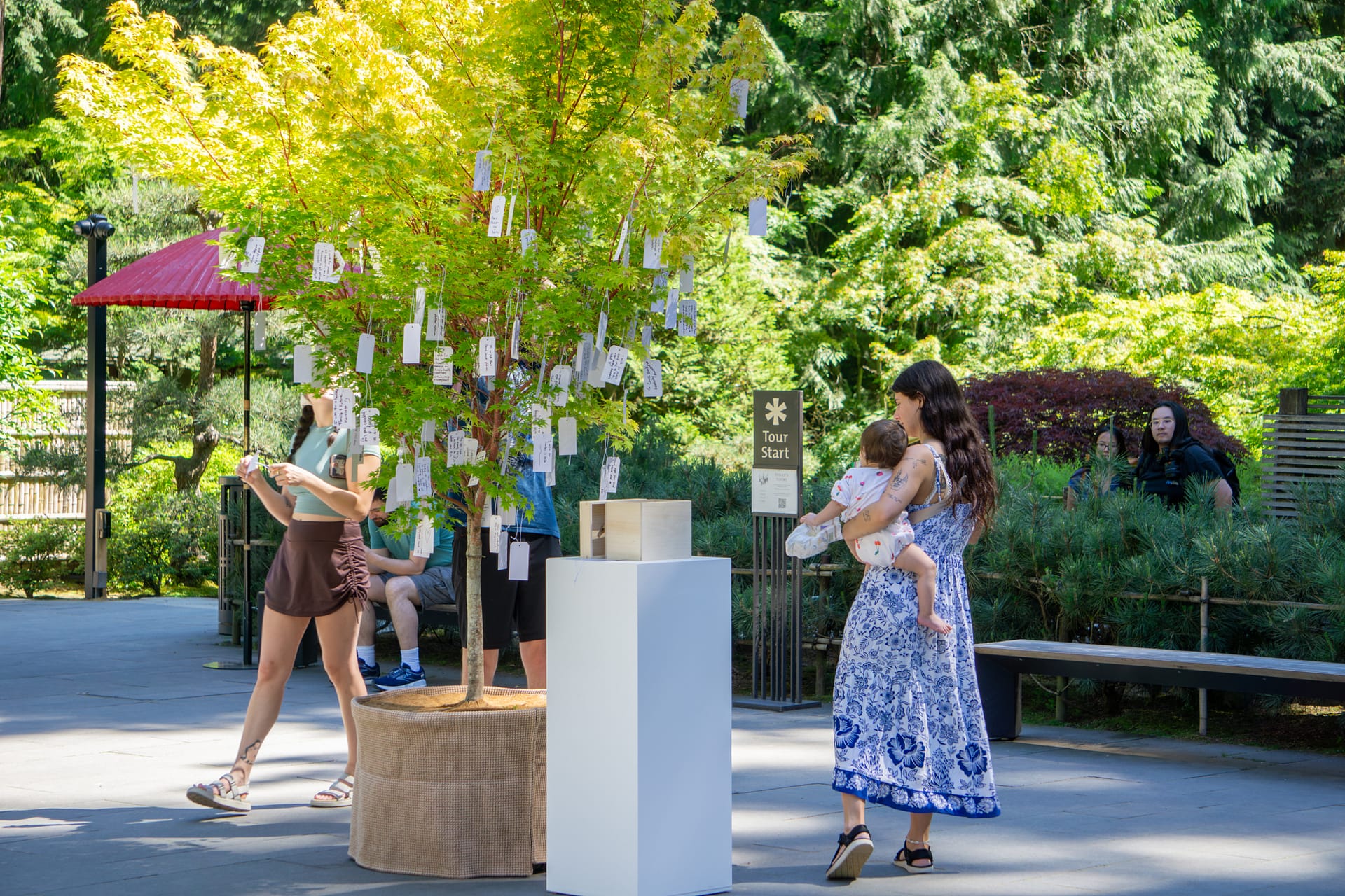 A mother holds her child in her arms as she looks at a tree with wishes hanging from it.