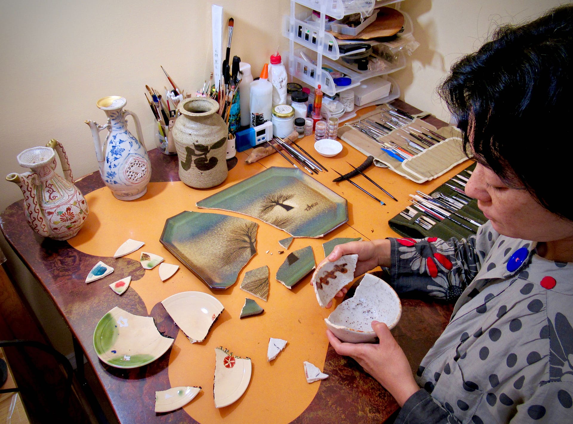 a woman piecing together broken pottery in her home studio