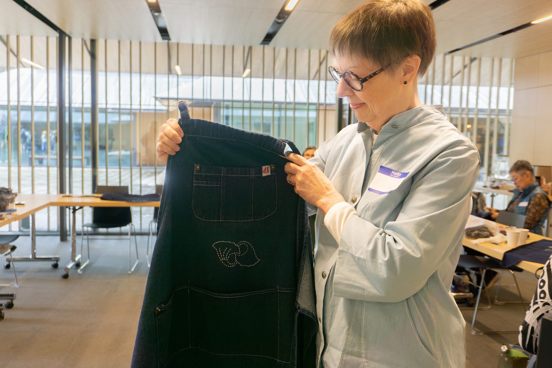 A woman holds a denim apron that she has embroidered designs on.