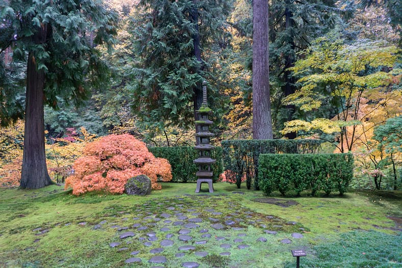 Stone pagoda lantern surrounded by moss, evergreens, and autumn foliage in shades of gold and orange at Portland Japanese Garden.