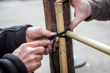 Two pairs of hands construct a bamboo fence