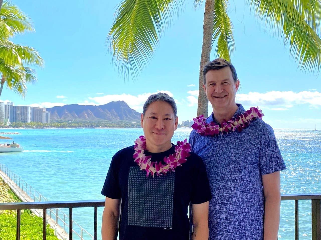 a couple stands in front of a body of water wearing lei