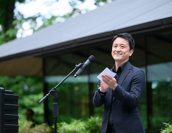 Aki Nakanishi standing at a microphone in Portland Japanese Garden.