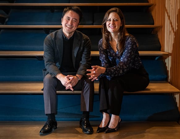 Two people sitting on wooden stairs, smiling for the camera.