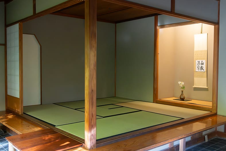 a tea room with tatami mats and an alcove with a flower in a vase in it and a scroll on the wall